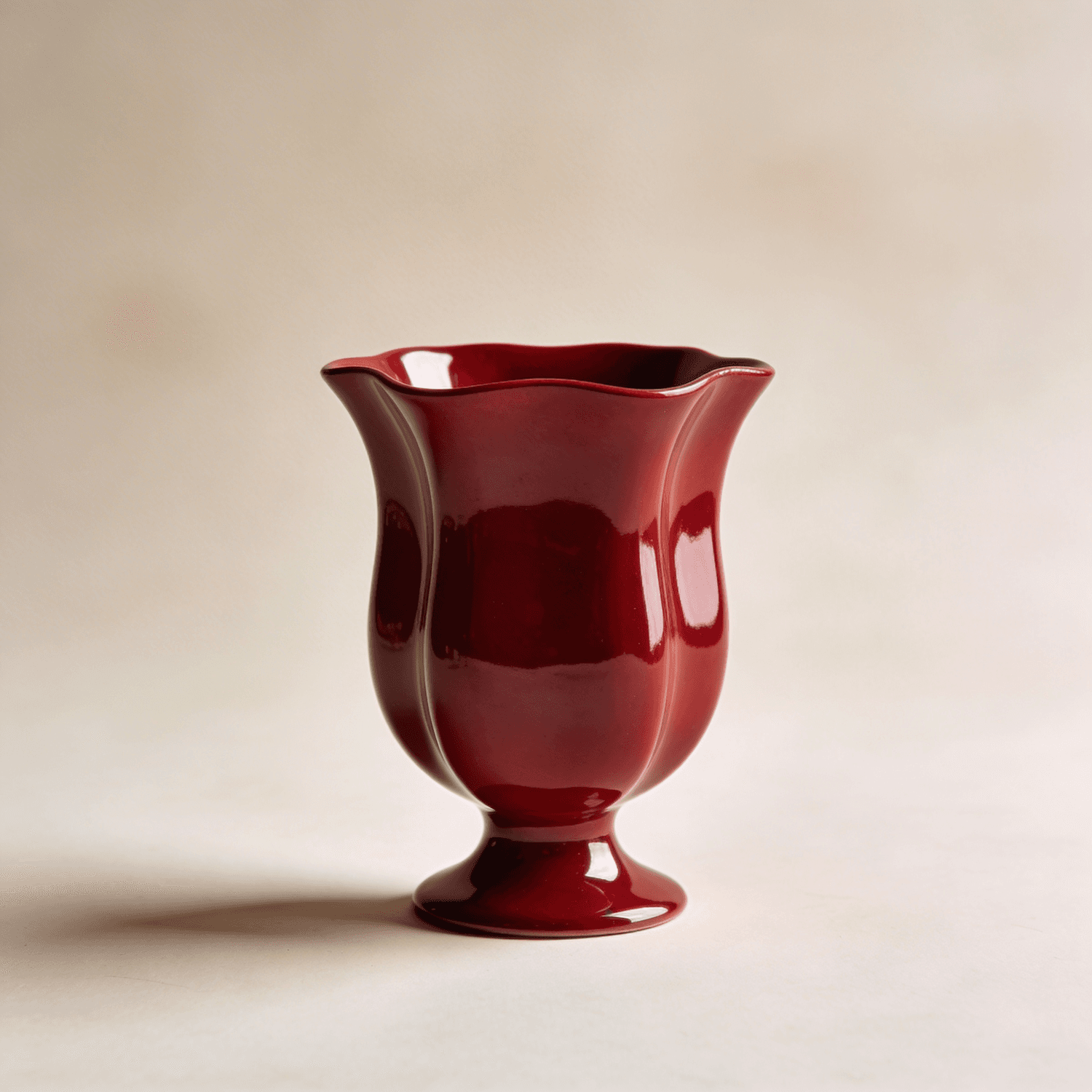 Glossy oxblood ceramic vase with a scalloped tulip rim and a pedestal base